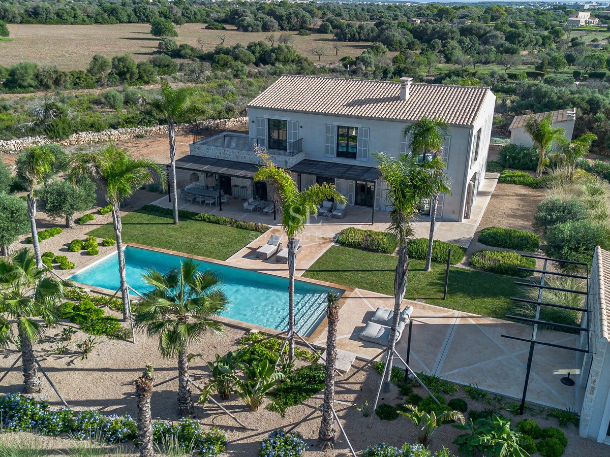Vue aérienne d'une villa de luxe avec piscine turquoise, palmiers et jardins paysagers.