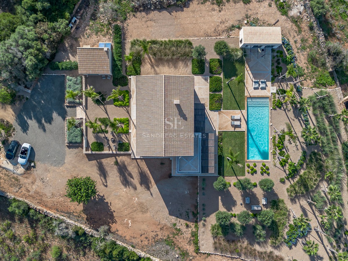 Vue à vol d'oiseau d'une villa moderne avec piscine turquoise, jardins paysagers et toits en terre cuite.
