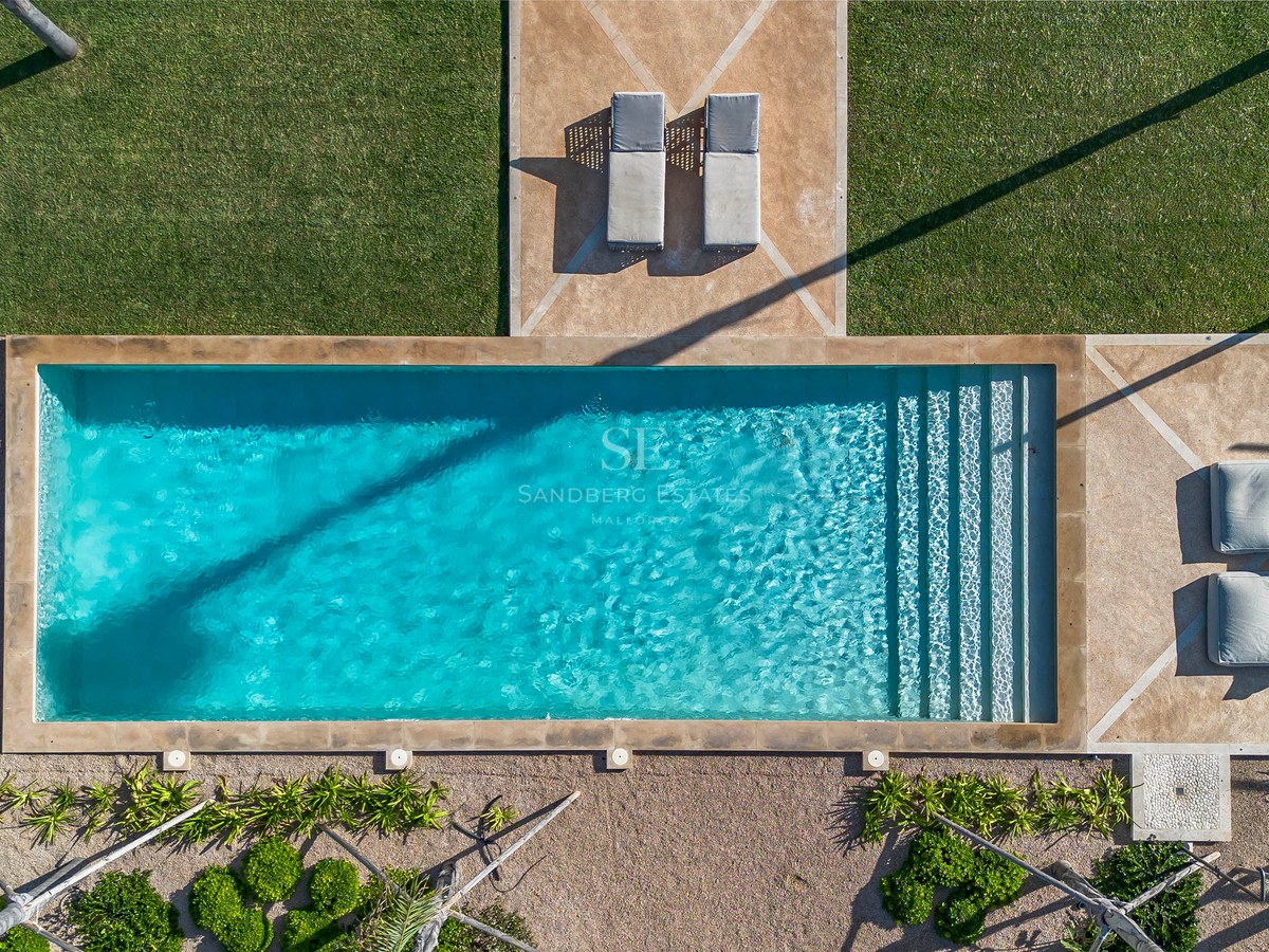Vue aérienne d'une piscine rectangulaire turquoise entourée d'une pelouse verte, de terrasses en pierre et de transats.