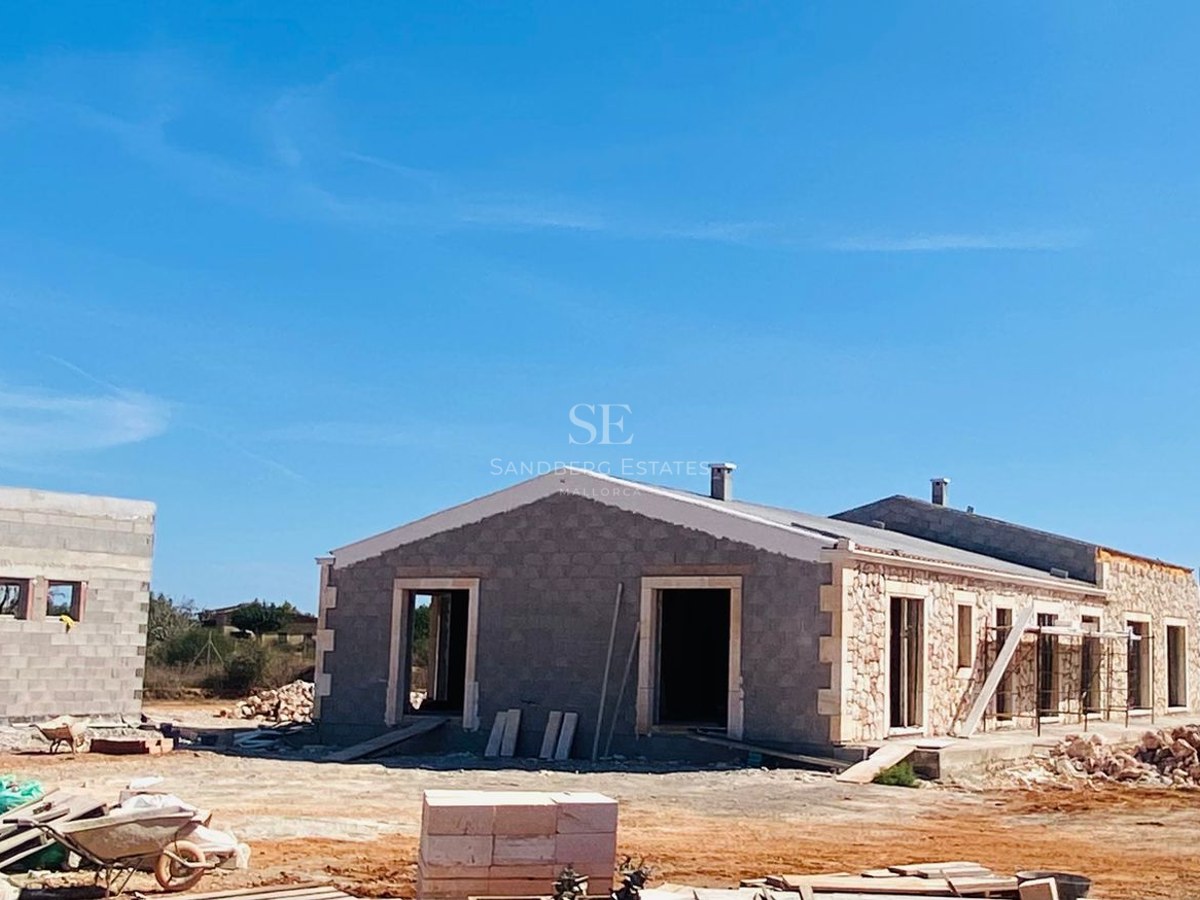Construction site of a modern Mediterranean villa with natural stone cladding under a clear blue sky.