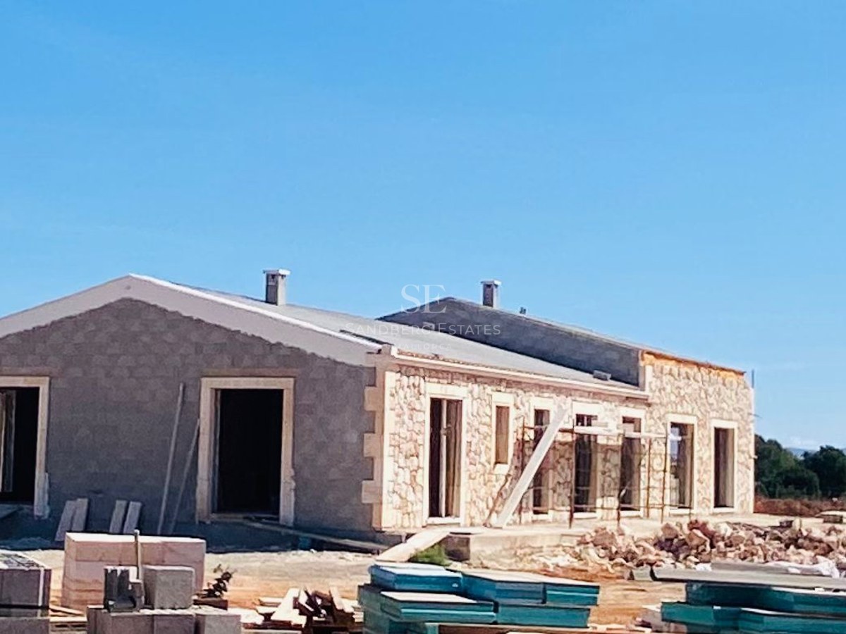 Exterior view of a luxury Mediterranean villa with natural stone cladding under construction against a clear blue sky.