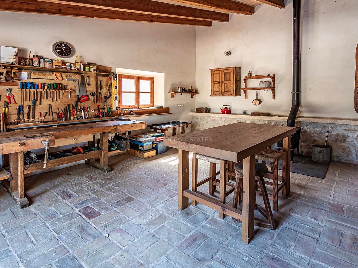 Atelier traditionnel avec un grand établi en bois, des outils au mur et des sols en pierre rustique.