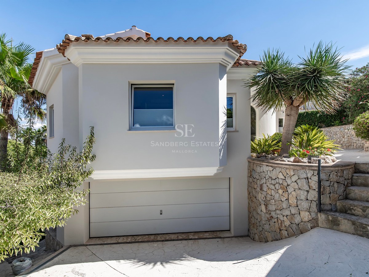 Façade de villa blanche avec mur en pierre naturelle, garage intégré et palmiers tropicaux.