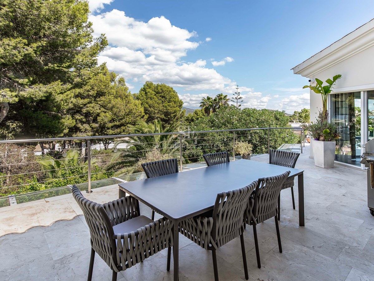 Terrasse extérieure avec salle à manger moderne, barbecue en inox et garde-corps en verre surplombant une forêt.