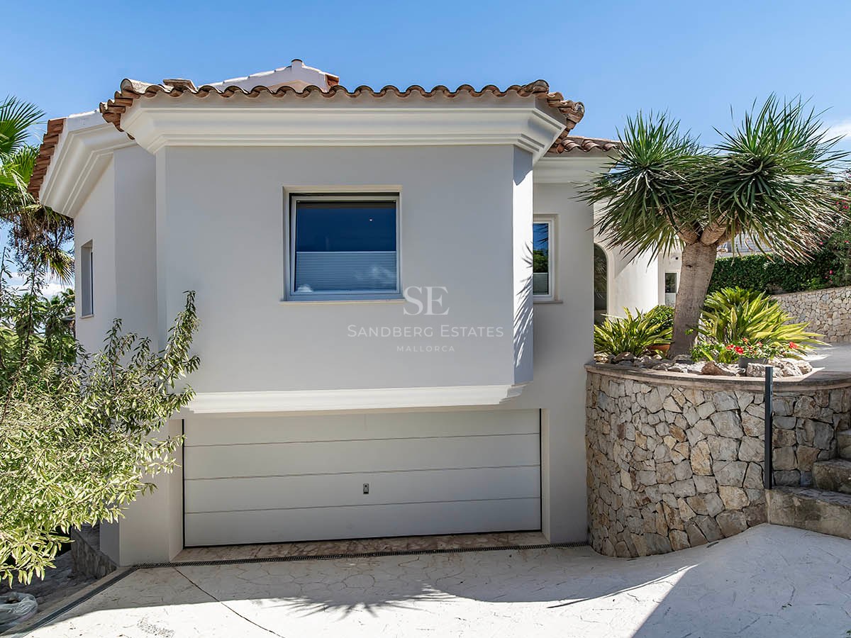 Extérieur de villa méditerranéenne blanche avec mur en pierre naturelle, garage intégré et aménagement paysager tropical.