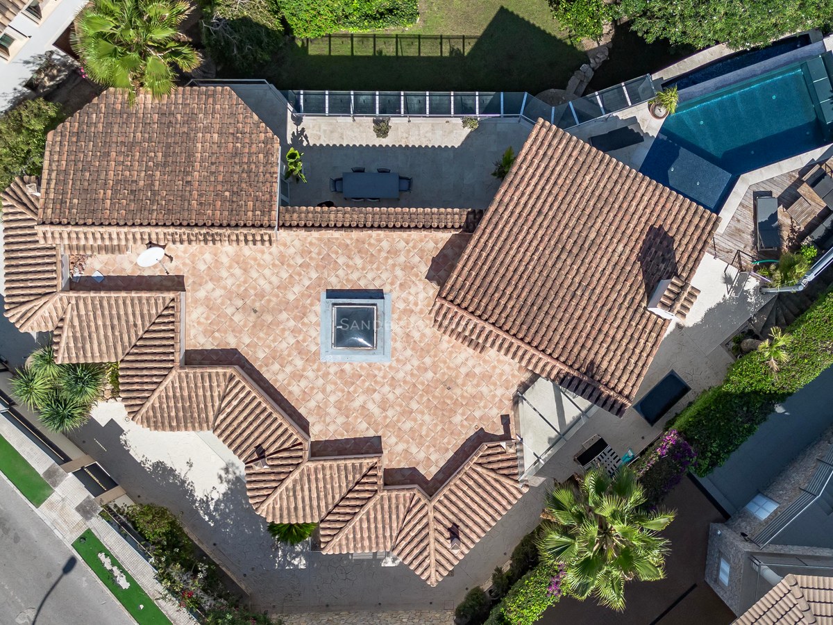Vue aérienne par drone d'une villa de luxe avec toits en tuiles, piscine privée et jardins paysagers.