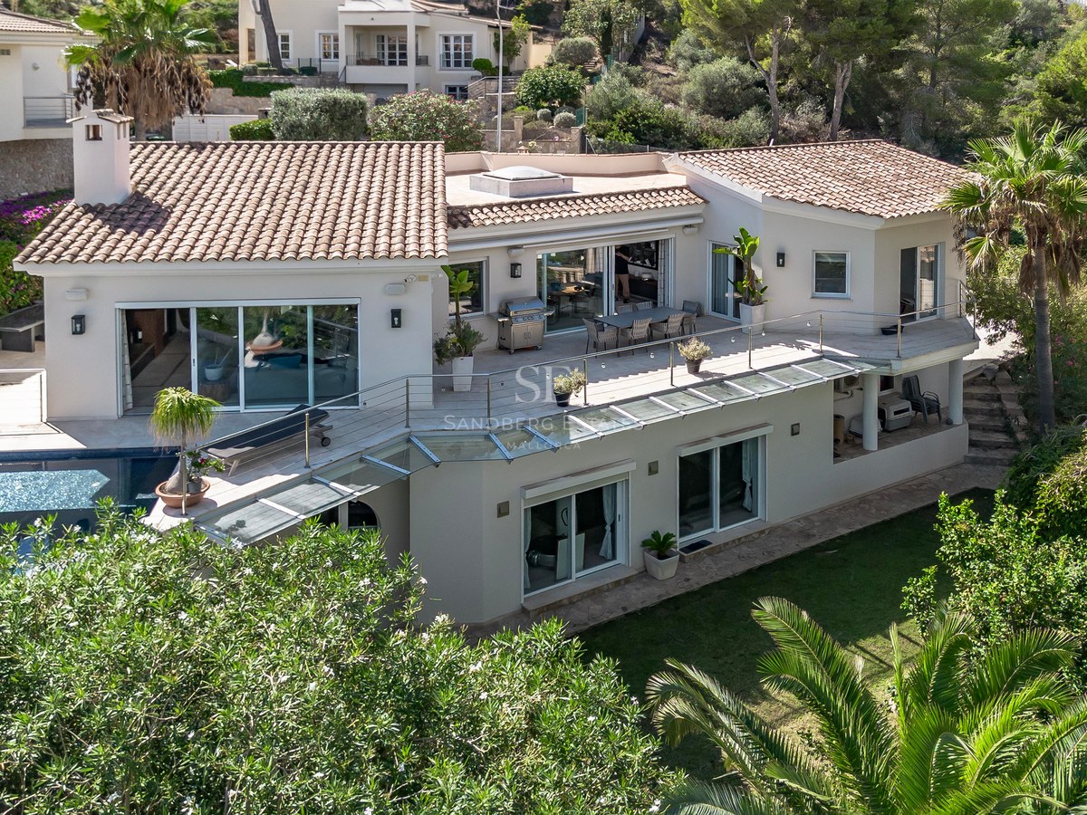 Vue aérienne d'une villa blanche à toit de tuiles, garde-corps en verre, grandes terrasses et piscine privée.