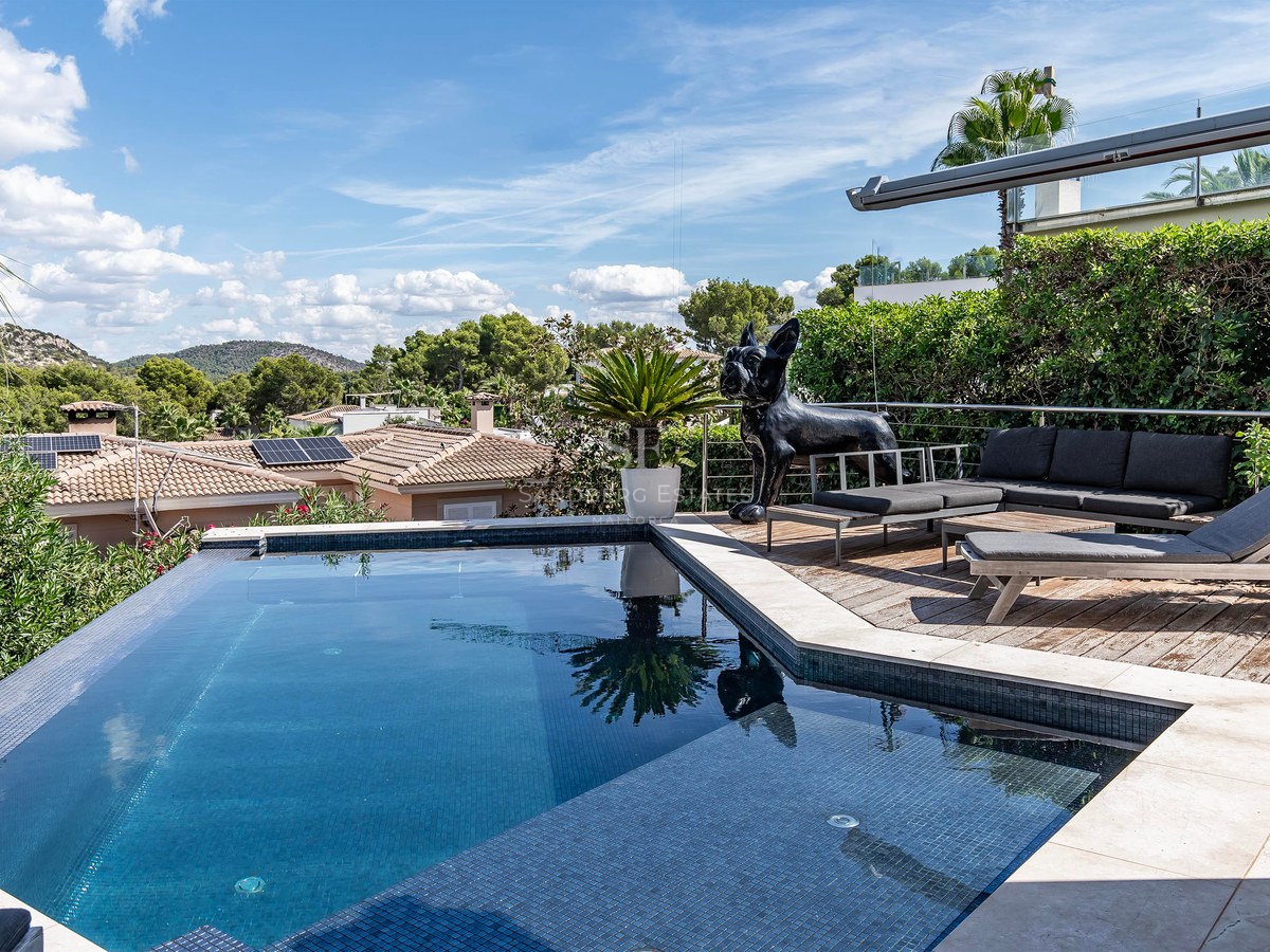 Piscine à débordement, terrasse en bois, mobilier moderne et vue sur les collines environnantes.