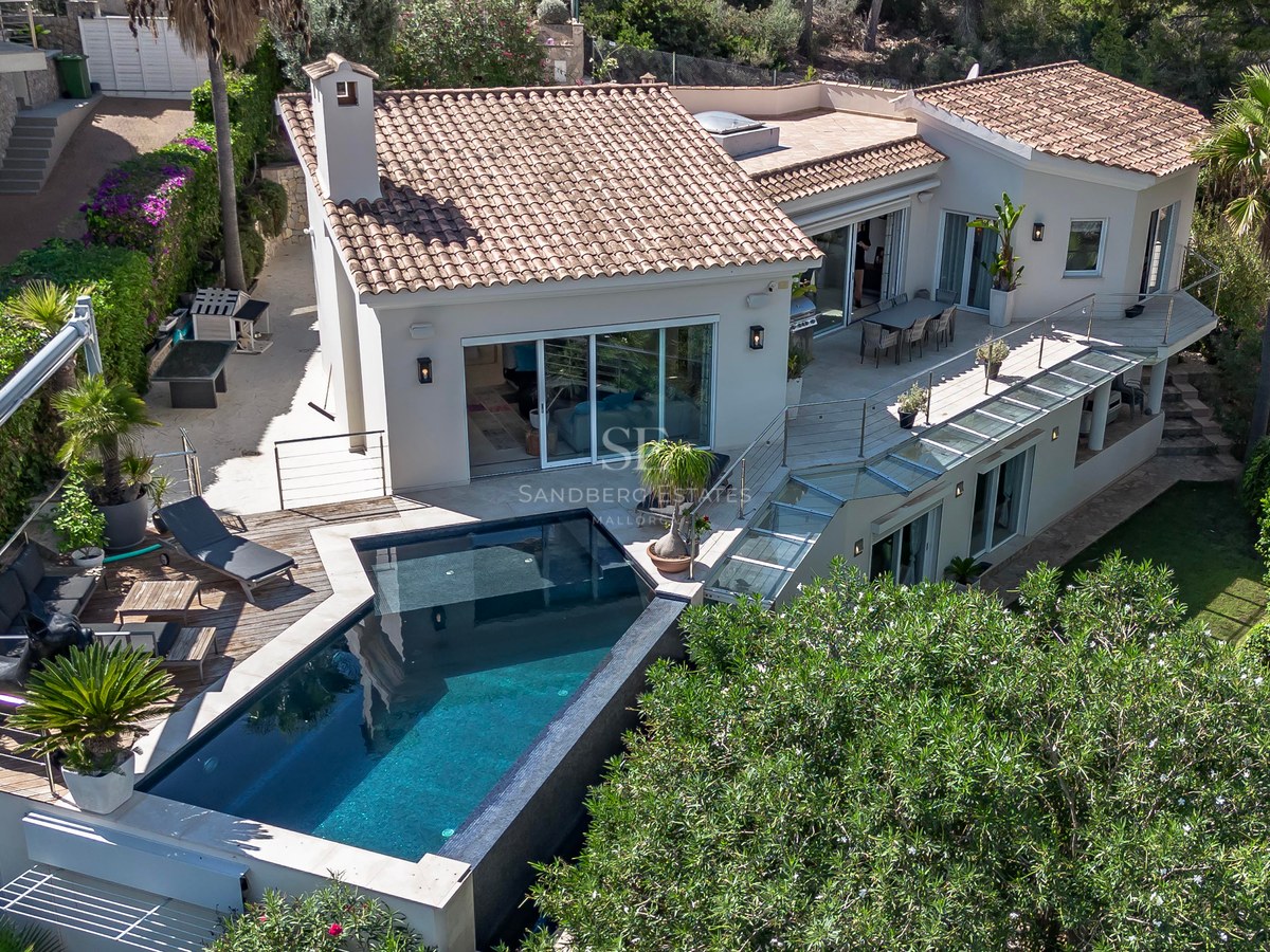 Vue aérienne d'une villa de luxe avec piscine carrelée sombre, terrasse en bois et paliers multiples.