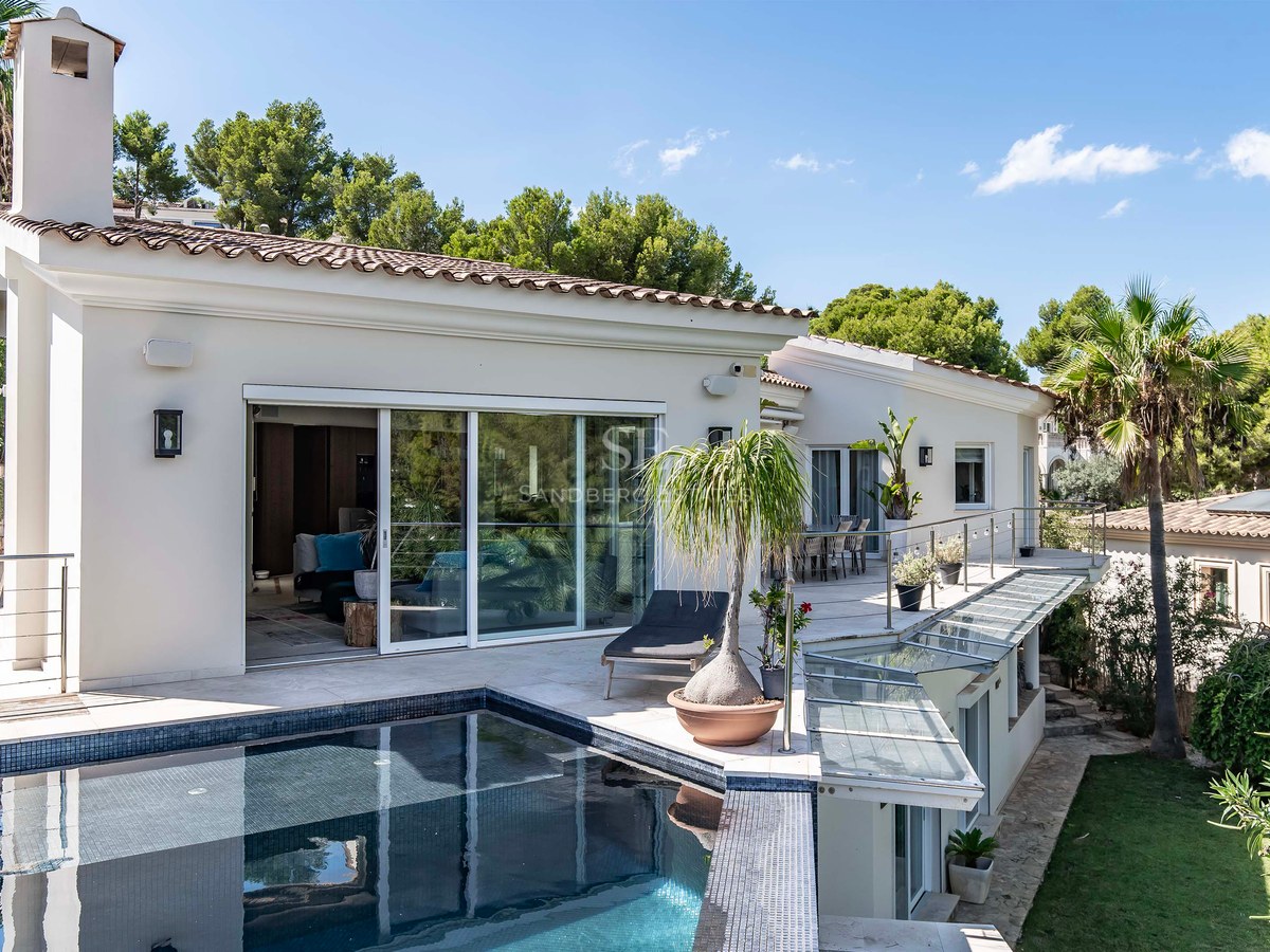 Vue en plongée d'une villa contemporaine blanche avec piscine carrelée sombre, terrasse vitrée et jardins luxuriants.