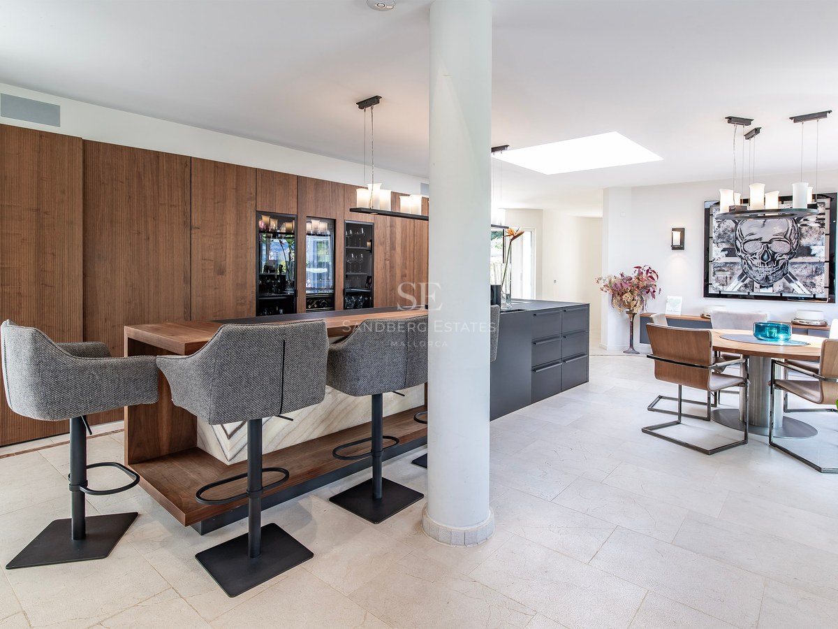 Cuisine moderne ouverte avec bar en bois, îlot gris, caves à vin et espace salle à manger contemporain.