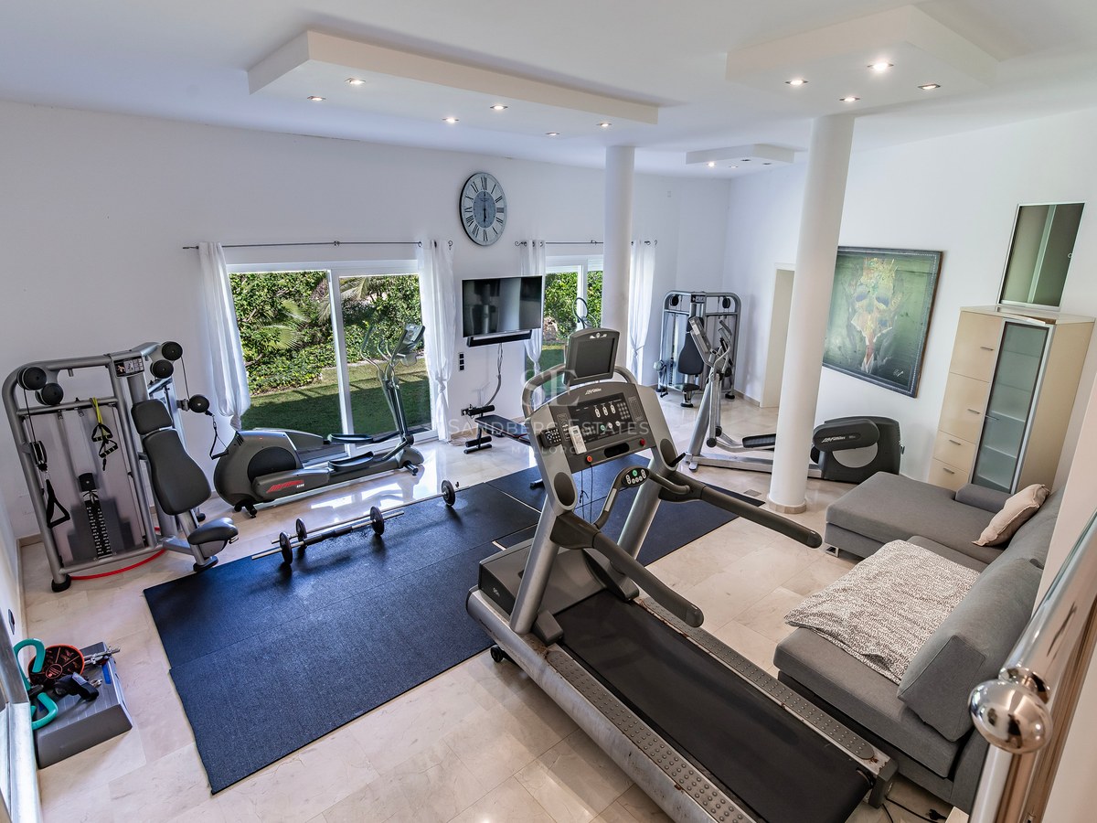 Salle de fitness à domicile spacieuse avec équipement professionnel, sol en marbre et accès extérieur.