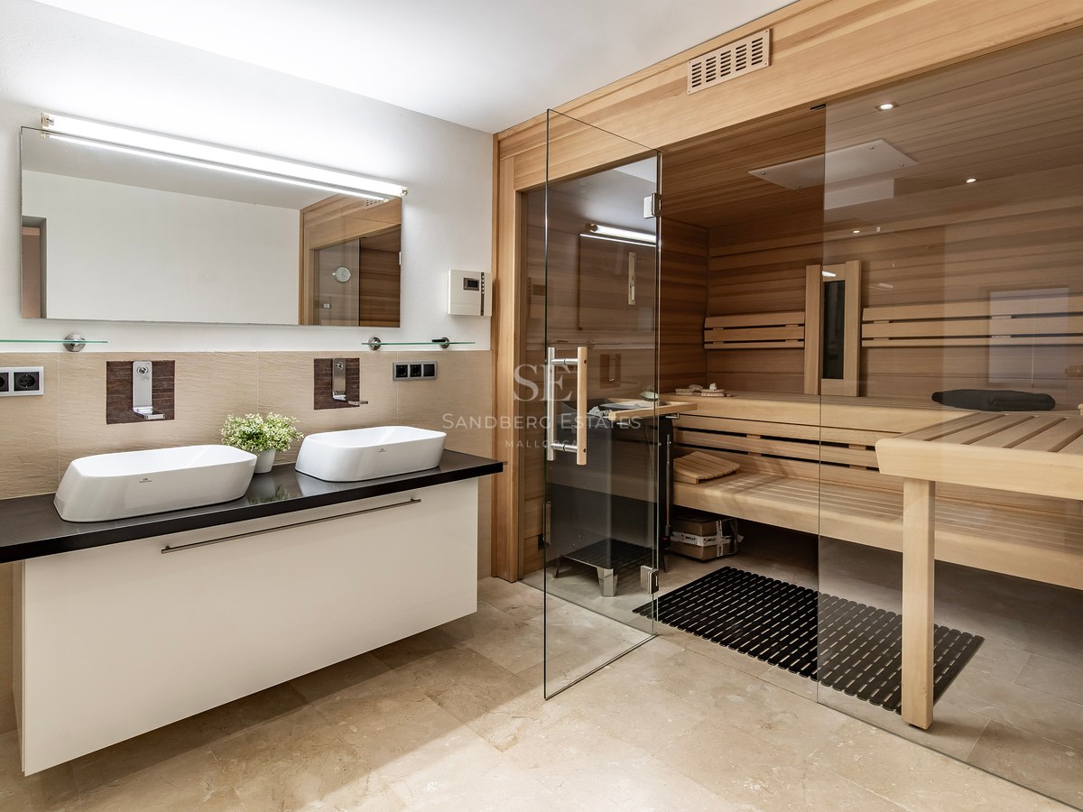 Salle de bain luxueuse avec sauna en bois intégré, porte vitrée et double vasque sur plan de travail noir.