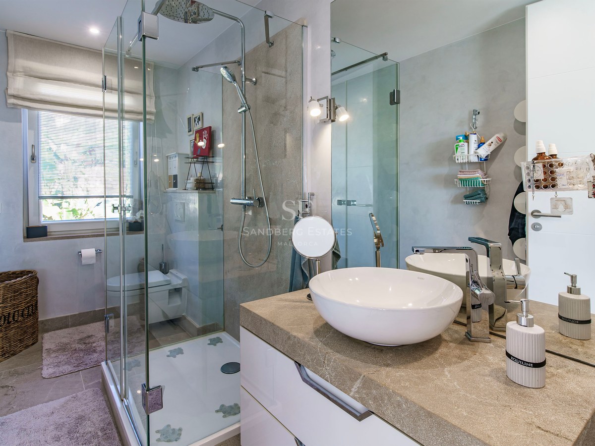 Baño contemporáneo con cabina de ducha de cristal, encimera de piedra natural y lavabo de diseño.