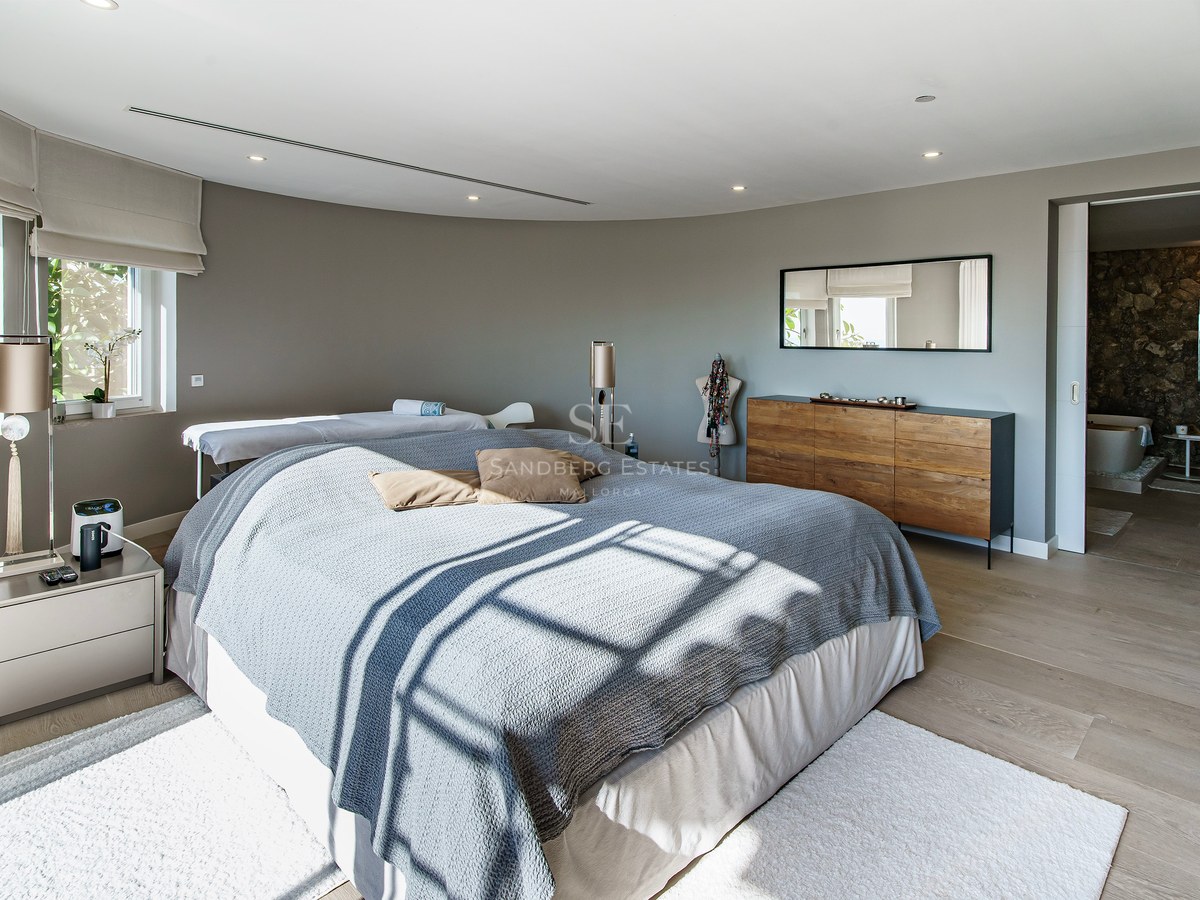 Dormitorio principal contemporáneo con ropa de cama gris, aparador de madera y vistas al baño privado con pared de piedra.