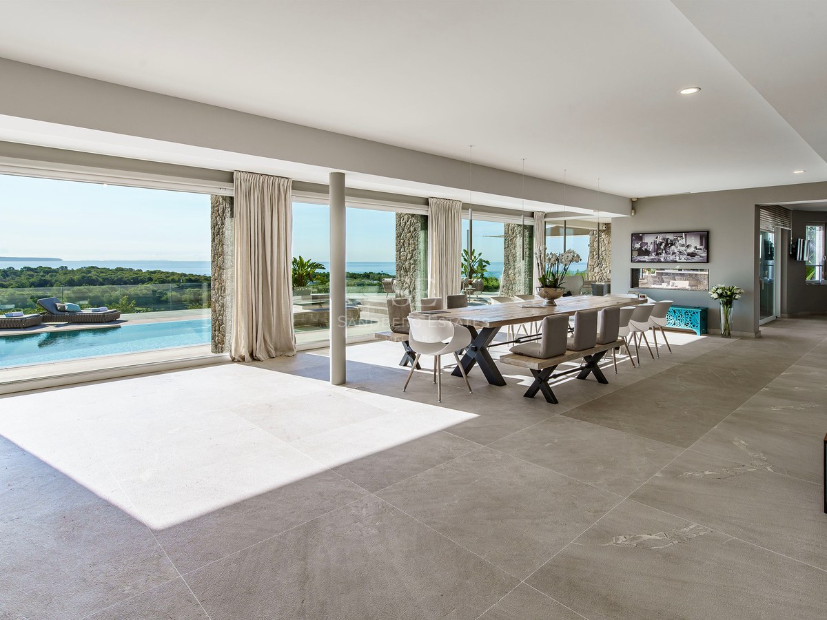 Comedor espacioso con ventanales de suelo a techo frente a una piscina infinita y vistas al Mediterráneo.
