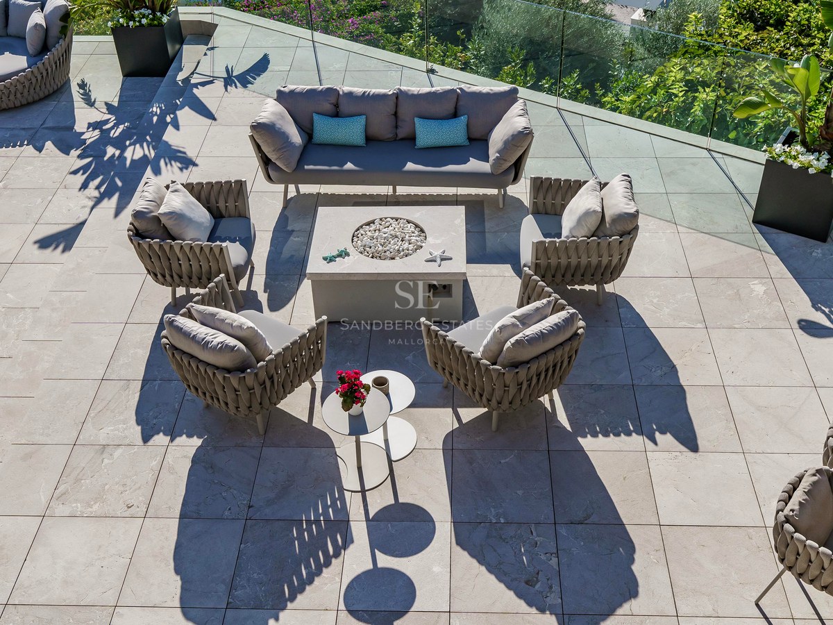 Vista aérea de una terraza de piedra con muebles de diseño, un brasero central y barandillas de cristal.