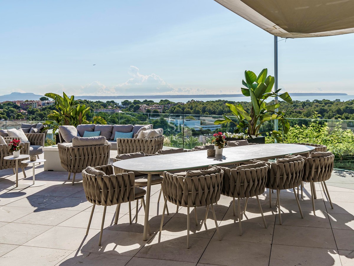 Terraza moderna con comedor, zona de estar, barandilla de cristal y vistas despejadas al mar y la costa.
