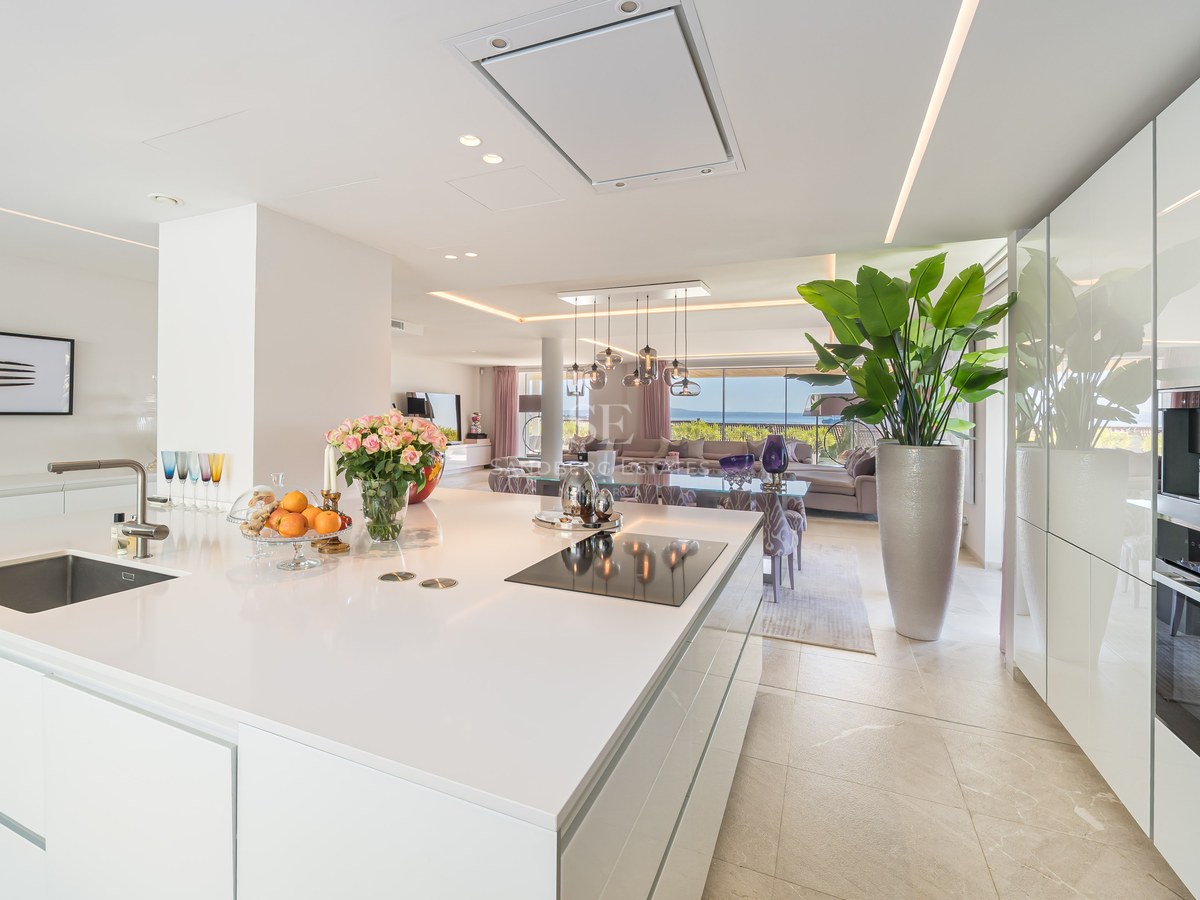 White kitchen island with induction hob, looking through to the living area and the Mediterranean sea beyond.