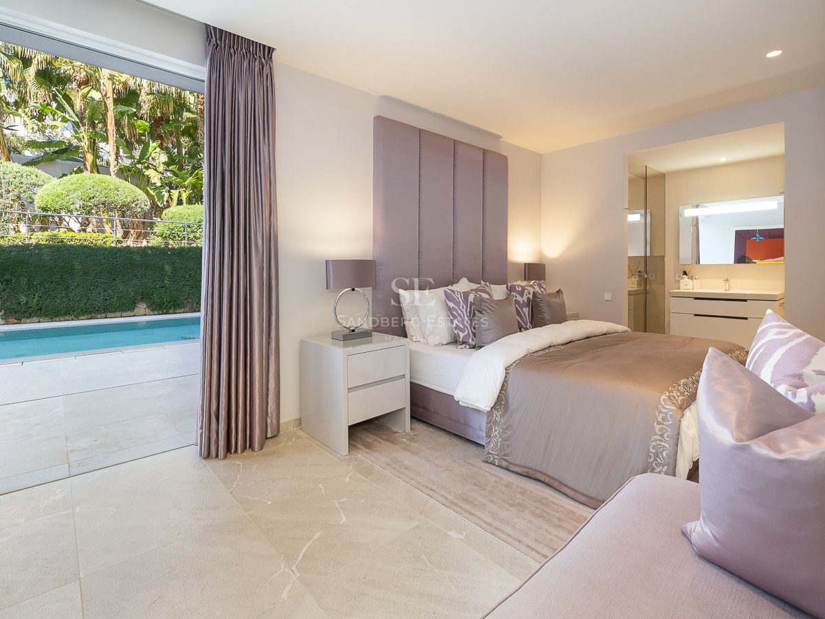 Modern bedroom with marble floors and large glass doors opening directly onto a private terrace and swimming pool.