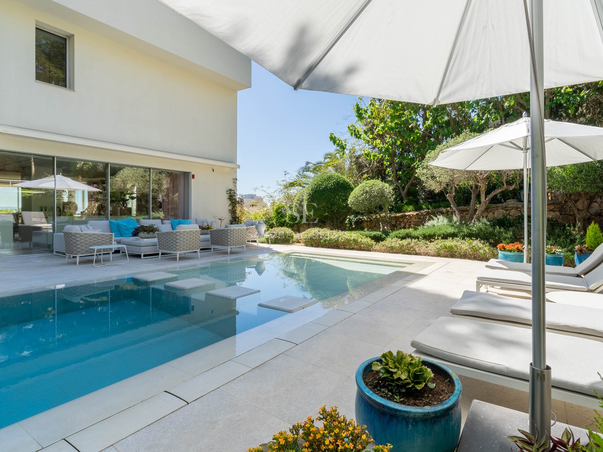 Modern rectangular swimming pool with stepping stones and white sun loungers on a natural stone terrace.