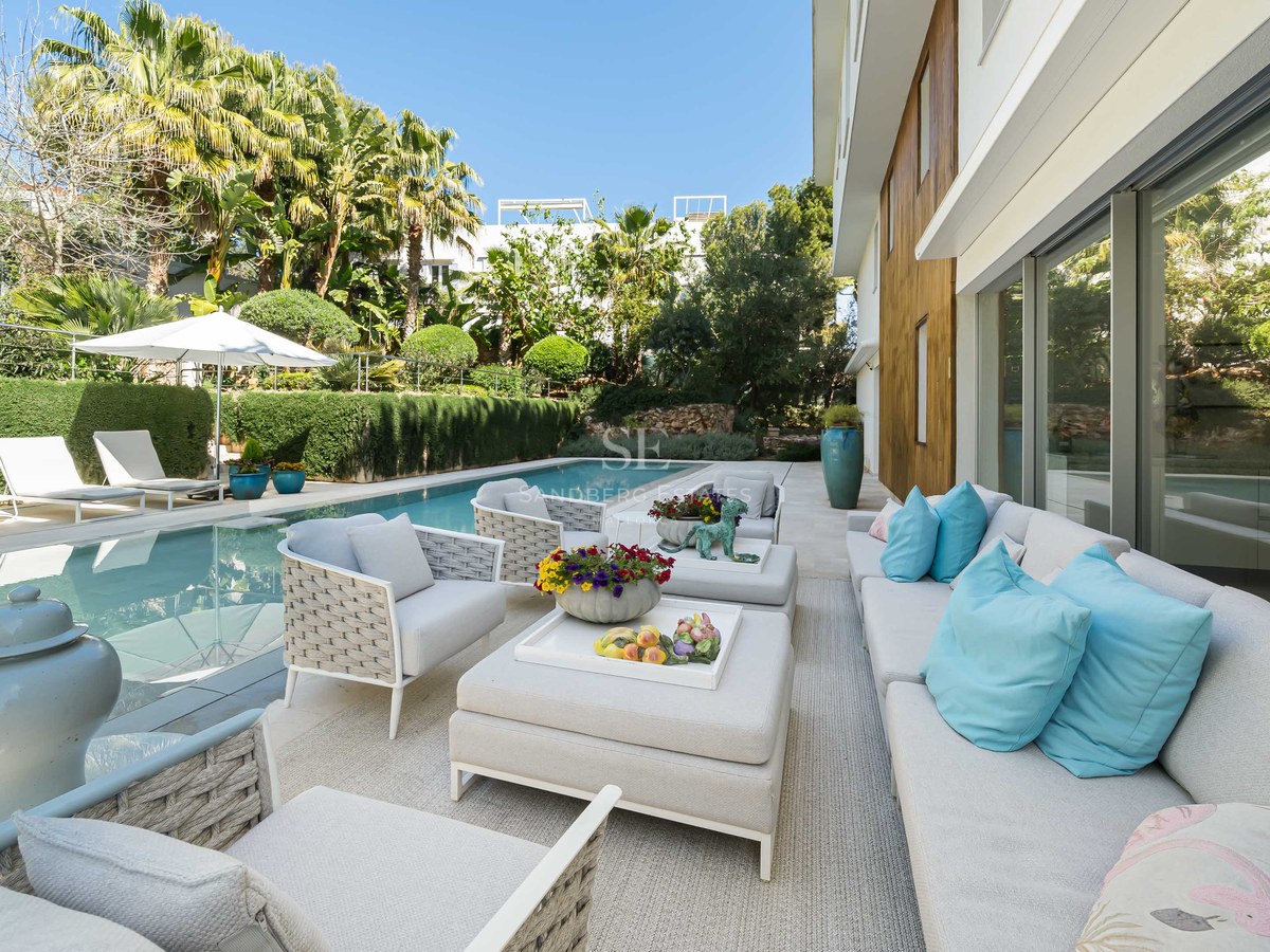 Luxury rectangular swimming pool alongside a stone terrace with white designer sofas, turquoise cushions, and lush palms.