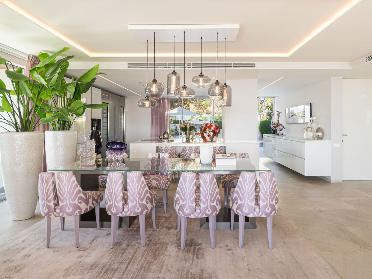 Contemporary dining room with a glass table, patterned lavender chairs, and designer glass pendant lighting.