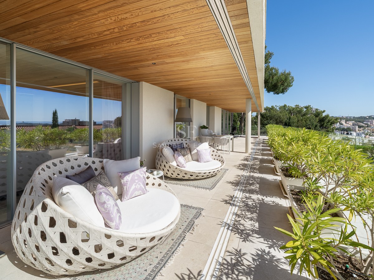 A long covered terrace featuring curved designer outdoor daybeds, wooden ceilings, and views over a Mediterranean town.