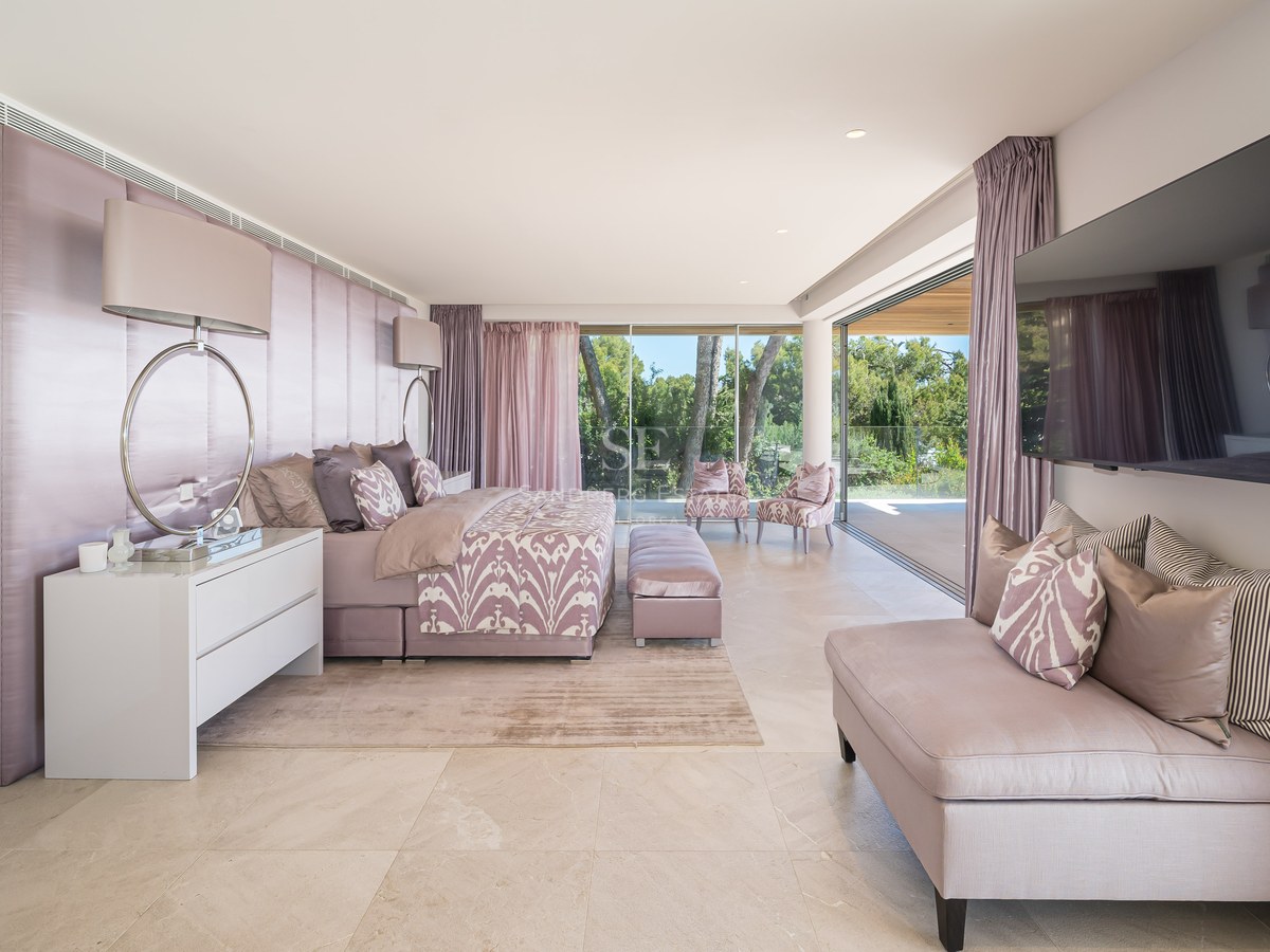 Spacious master bedroom featuring natural stone floors, a mauve upholstered headboard, and sliding doors to a terrace.