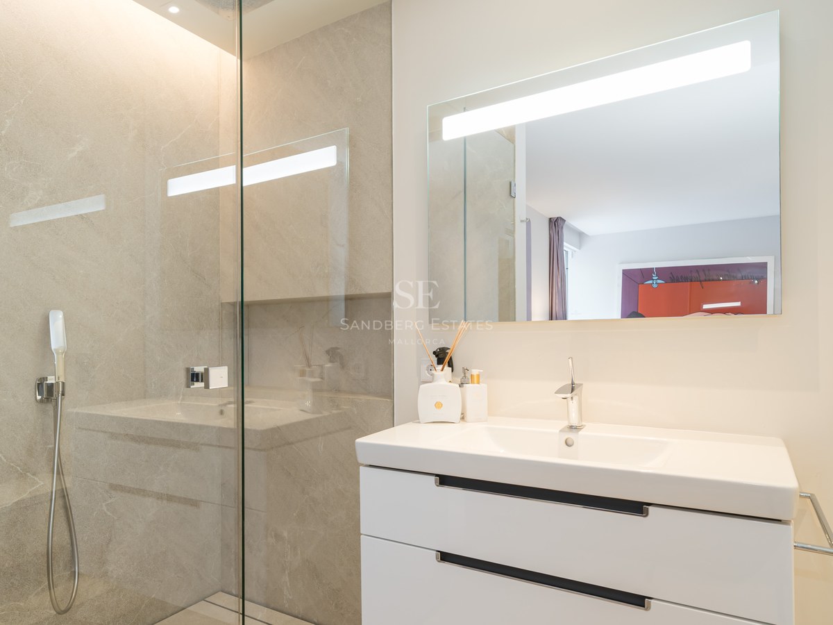 Modern bathroom featuring a glass walk-in shower, white floating vanity, and a large backlit LED mirror.