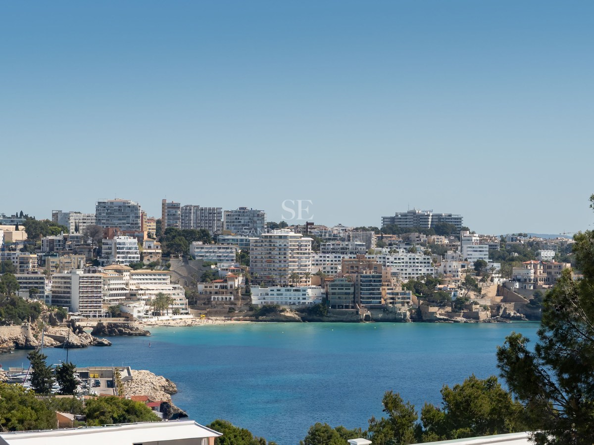 Elevated view of a turquoise bay surrounded by white coastal architecture and lush greenery under a clear blue sky.