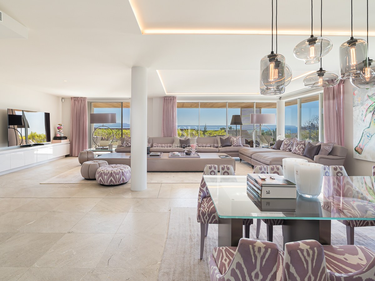 Bright open-plan living and dining room with marble floors and large windows overlooking the sea and coastline.
