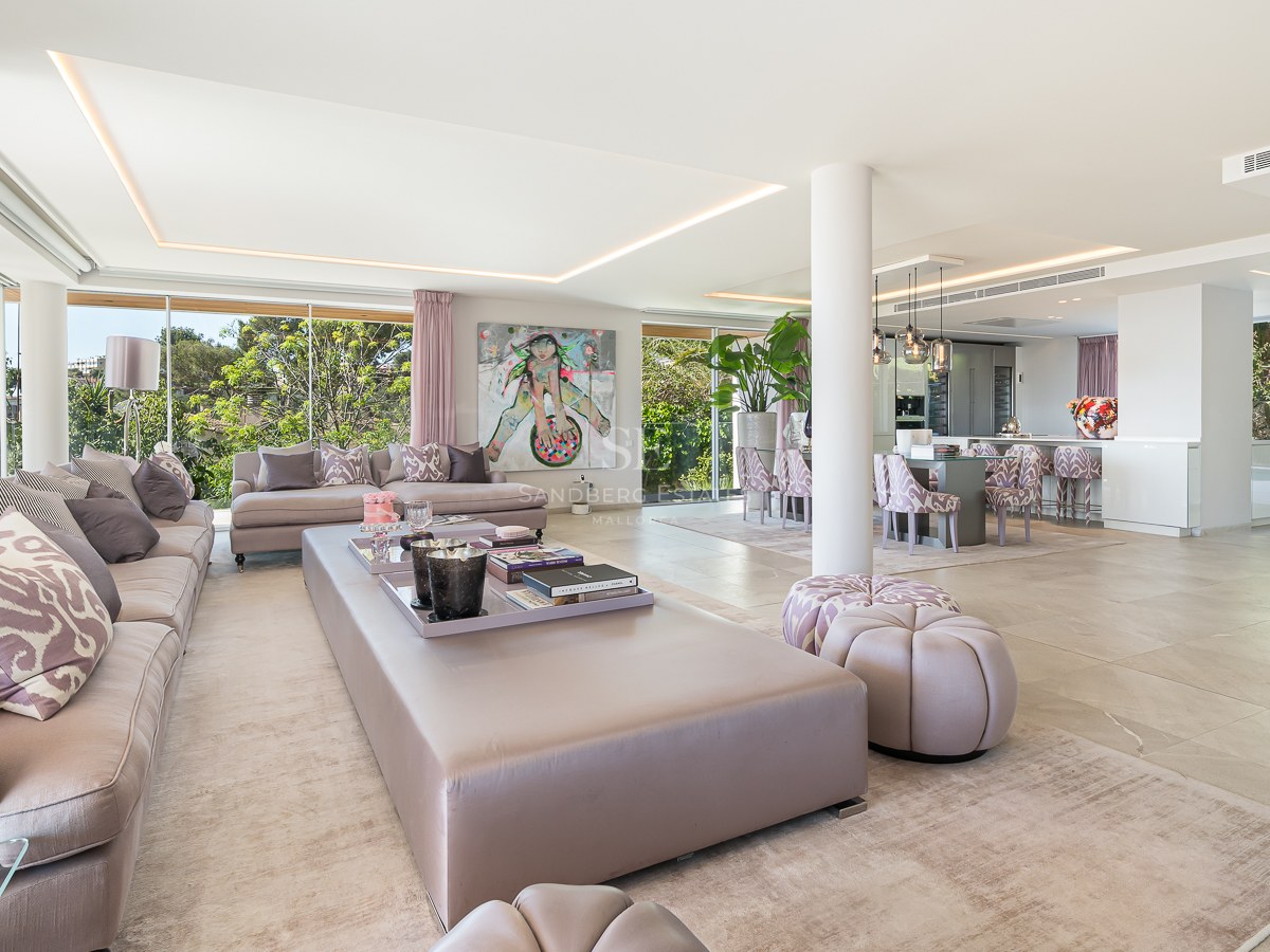 Spacious modern living room with plush grey sofas and floor-to-ceiling windows overlooking lush greenery.