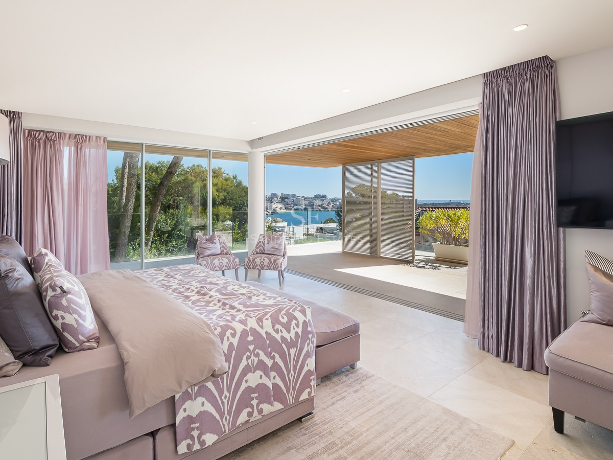 Modern bedroom with lavender accents and king bed, opening onto a sun-drenched terrace with Mediterranean coastal views.