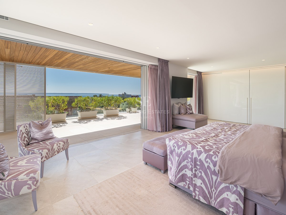 Spacious master bedroom with lavender accents opening onto a sun-drenched terrace with coastal views and wooden pergola.