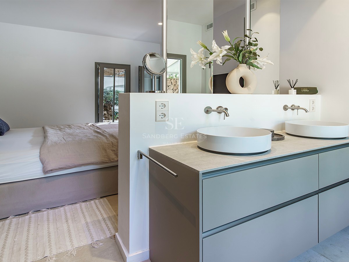 Dormitorio principal de planta abierta con tocador doble, dos lavabos sobre encimera y una cama grande con cojines azules.