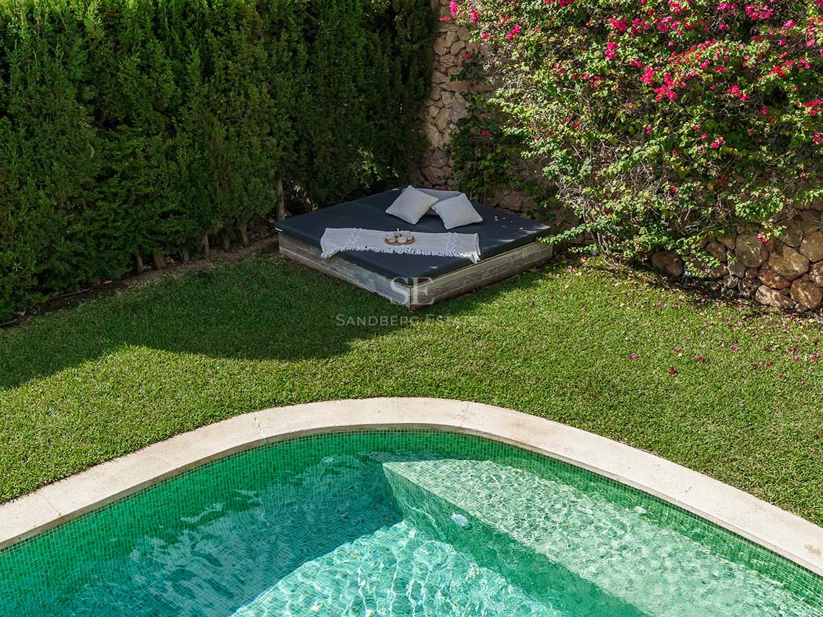 Piscina de azulejos verdes junto a un césped cuidado y una cama balinesa bajo flores de buganvilla.