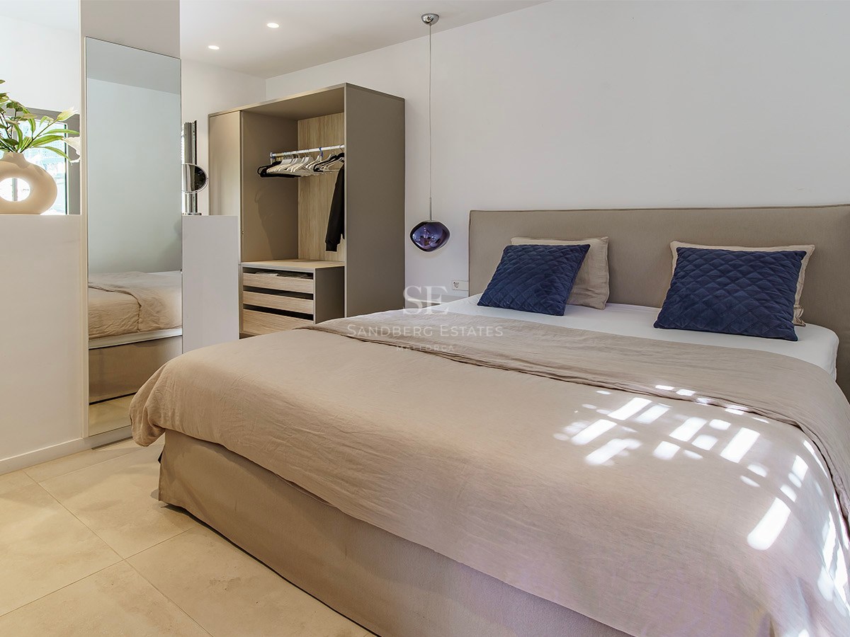 Habitación moderna y luminosa con cama beige, cojines azules, lámparas colgantes de cristal morado y espejos grandes.
