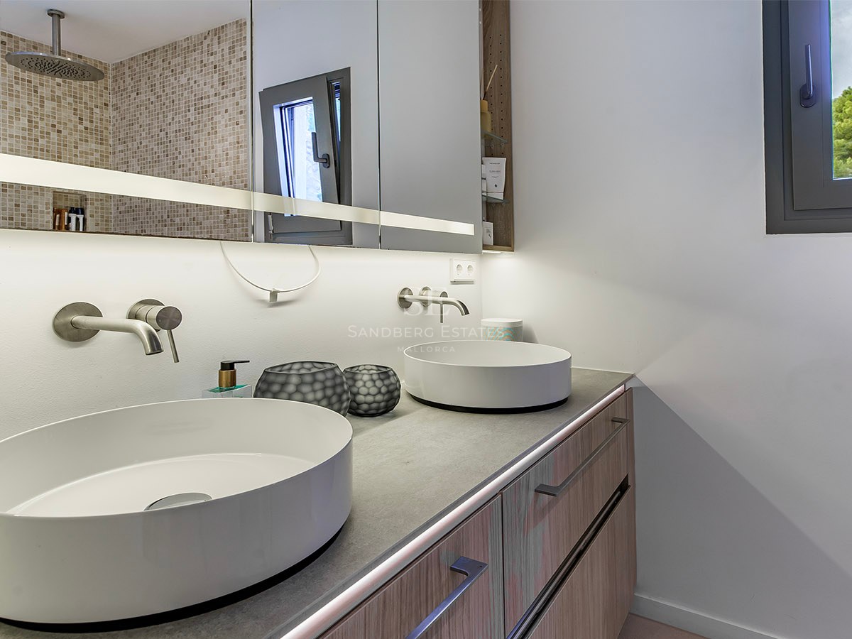 Baño moderno con dos lavabos blancos sobre encimera gris, muebles de madera y gran espejo iluminado.