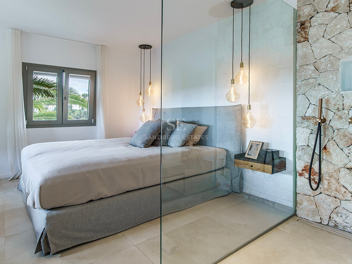 Dormitorio contemporáneo con cama gris, pared de cristal y ducha de piedra rústica con grifería de latón.