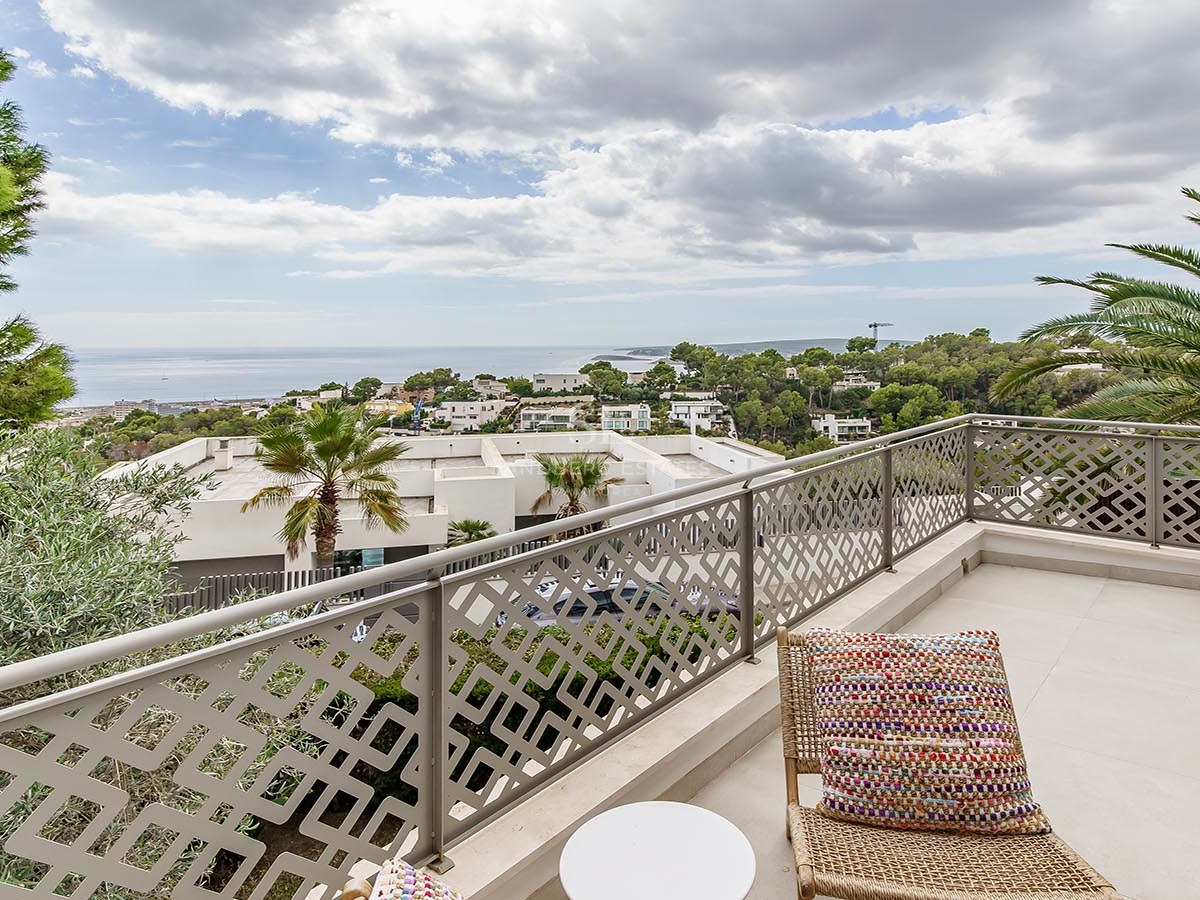 Balcón moderno con barandilla decorativa, silla de mimbre y vistas a la costa mediterránea bajo un cielo nublado.