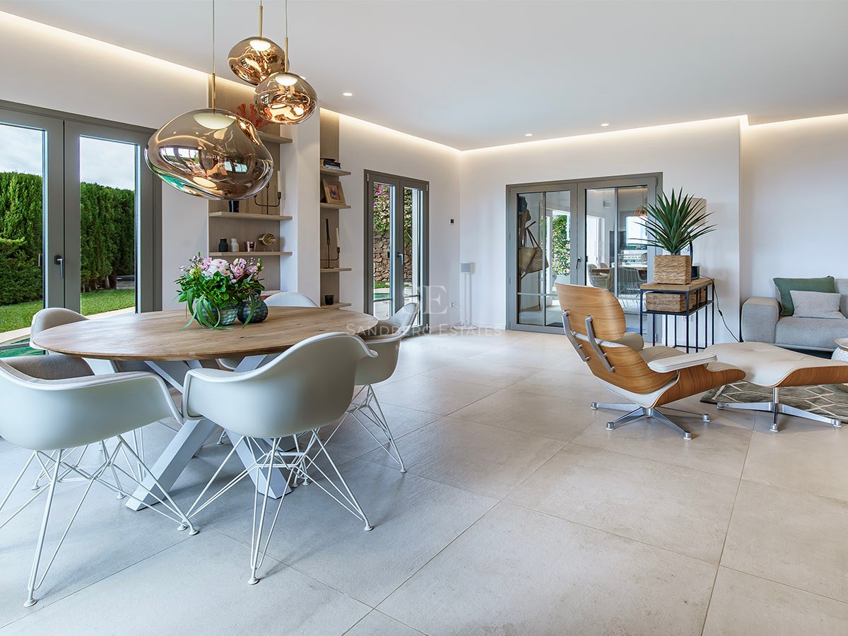 Salón moderno con comedor, sillas de diseño, lámparas de cobre y sofá gris con acceso al jardín.