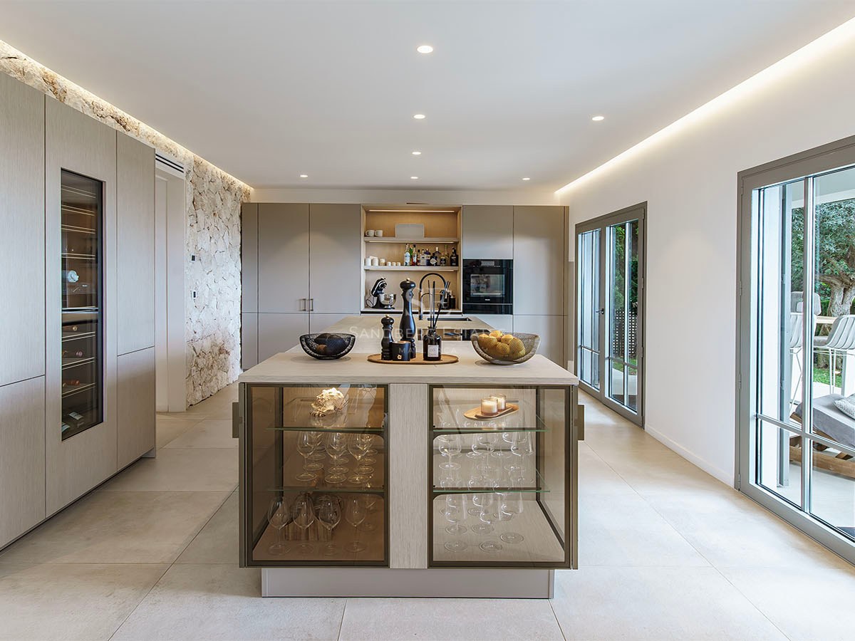 Cocina contemporánea con isla de madera, vinoteca integrada, pared de piedra natural y puertas de cristal al jardín.