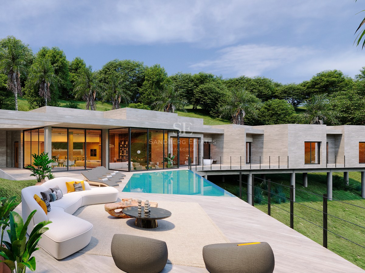 Contemporary villa terrace featuring a turquoise pool, white curved sofa, and glass walls against a lush hill.