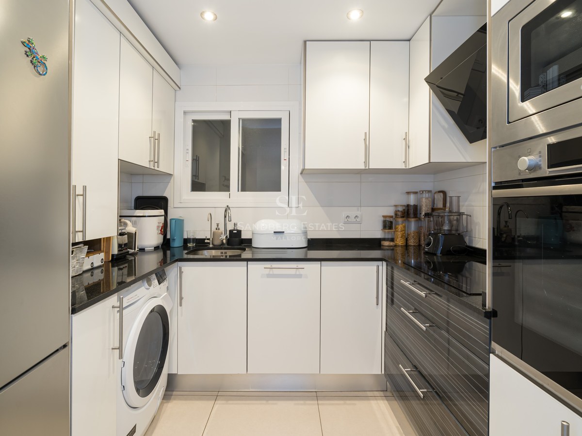 Cocina moderna en forma de U con armarios blancos, encimeras negras y electrodomésticos de acero inoxidable.