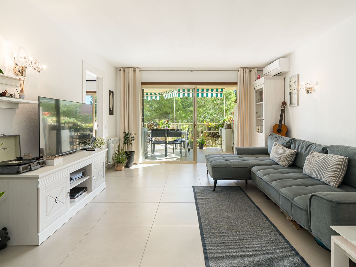 Salón moderno con sofá azul, mueble de TV blanco y puertas correderas que dan a una terraza con vegetación.