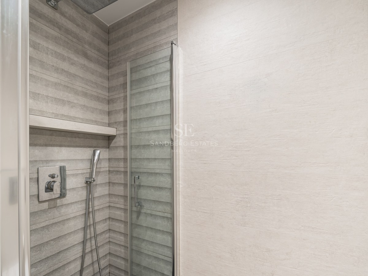 Ducha moderna con azulejos grises texturizados, puerta de cristal y grifería de cromo.