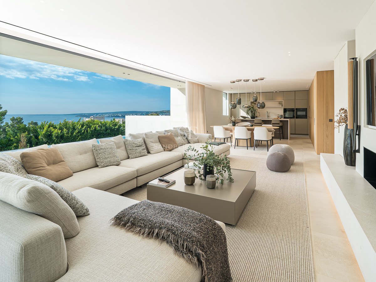 Vaste salon moderne avec canapé d'angle, grandes baies vitrées et vue dégagée sur l'océan et la verdure.