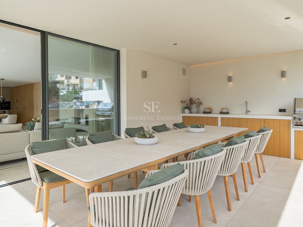 Grande table à manger extérieure avec dix chaises à côté d'une cuisine d'été professionnelle sur une terrasse couverte.