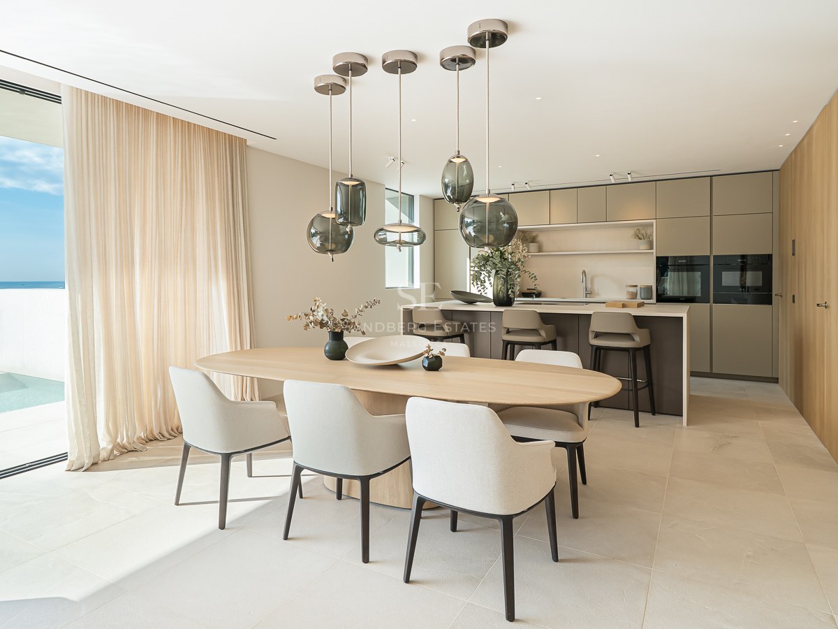 Salle à manger contemporaine avec table en bois et suspensions en verre, surplombant une piscine et la mer.